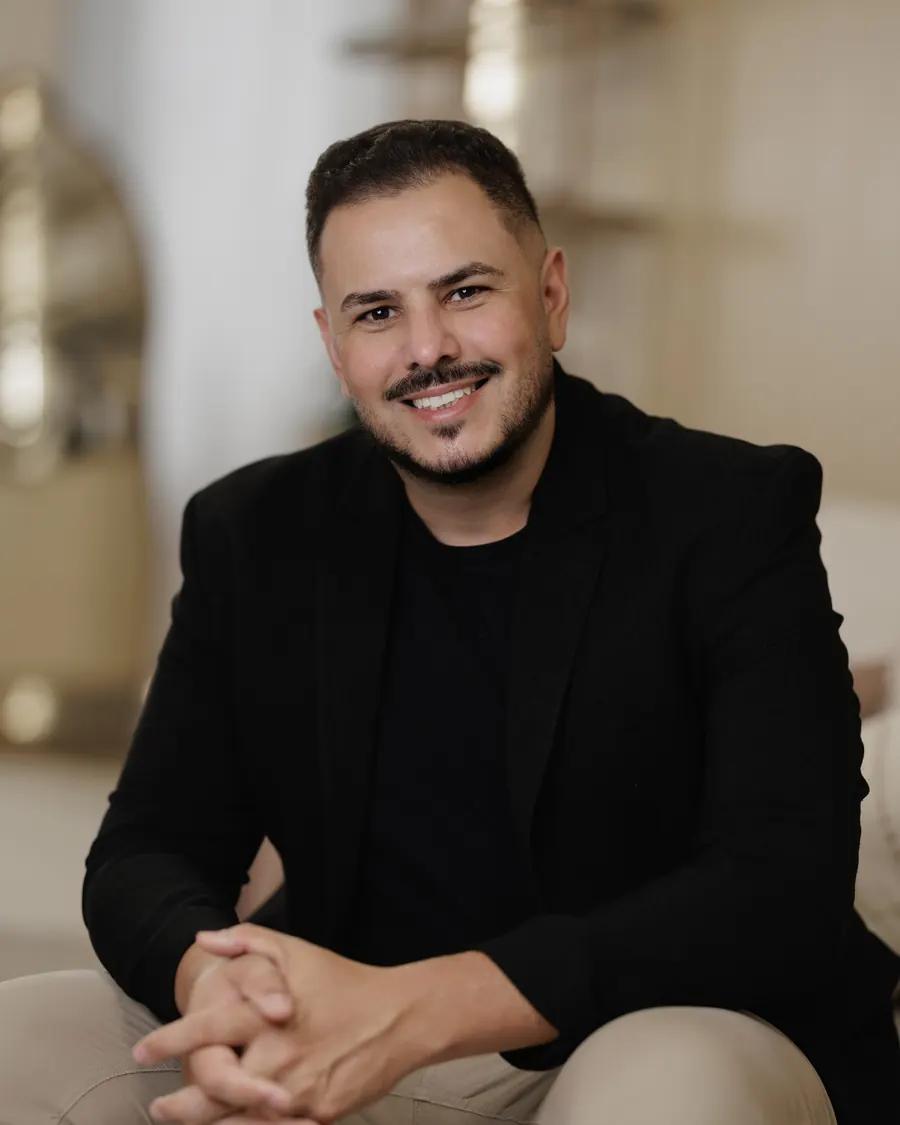 Retrato de Bruno Santos sentado, de blazer preto, em ambiente claro